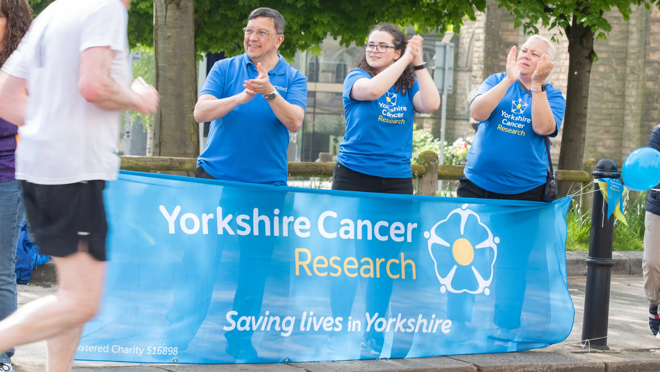 A group of people in front of a Yorkshire Cancer research banner clap passing runners.