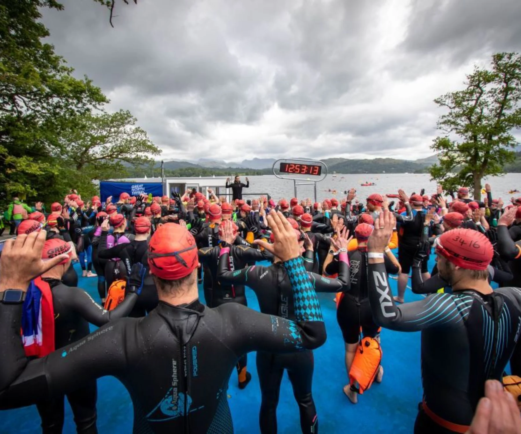 Swimmers in wetsuits warm up on the shore of a lake
