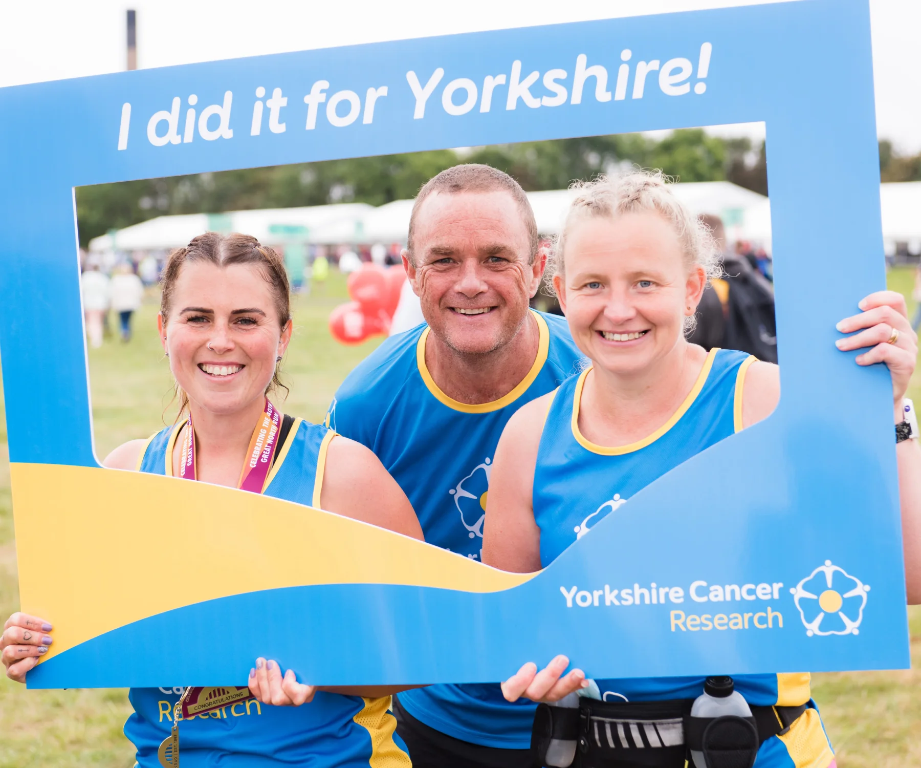 Three people wearing Yorkshire Cancer Research running vests and holding up a giant frame that reads "I did it for Yorkshire!"